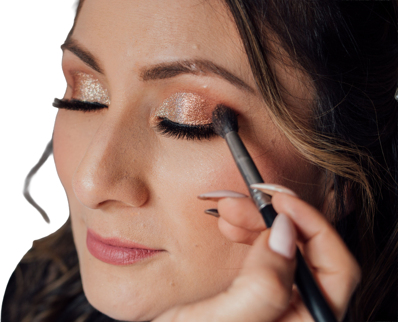 Close-up of a closed eye with shimmery champagne shadow on the lid, while a brush applies a deeper warm-brown transition into the crease — the exact moment a flat wash turns into a dimensional eye